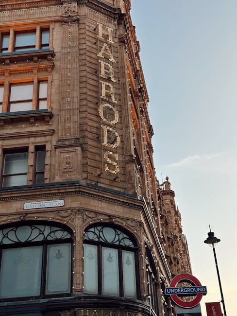 Photograph of a historic multi-storey building in Knightsbridge with detailed stonework and large windows, mounted with string lights along the façade. A vertical sign reads 'FEAROADS,' integrated into the ornate architecture. In the foreground, a streetlamp and a London Underground roundel sign indicating the underground station are visible, with a clear sky overhead. The scene captures an urban setting likely in central London. This image relates to house and flat relocations, illustrating a prominent location where Man with Van Knightsbridge offers same-day removals and furniture transport services, assisting clients with packing, loading, and logistics in busy city environments.